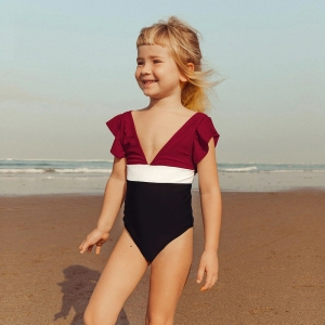 Leende blond tjej på stranden iförd en baddräkt i ett stycke