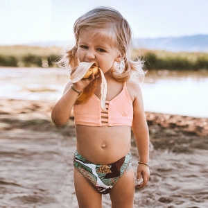 Tvådelad baddräkt för flicka som bärs av en liten flicka på stranden.