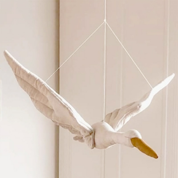 Docka i form av en vit svan med beige näbb hängande i tre snören framför en vit vägg