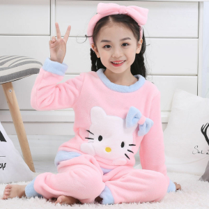 Hello Kitty vinterpyjamasset i fleece för flickor som bärs av en liten flicka med ett moderiktigt pannband i ett hus