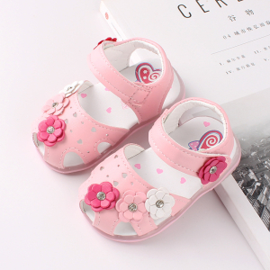 Rosa sandal för flickor med 4 små blommor i olika färger, placerade på en tidning och ett vitt bord