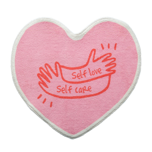 Hjärtformad sovrumsmatta för flickor i rosa. På ovansidan ett tryck av två händer med orden self love self care i rött.