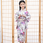 framför en japansk skärm bär en liten flicka en traditionell vit kimono med ett rosa blommotiv
