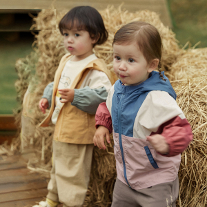 En pojke och en flicka klädda i en färgglad parkas står bredvid en halmbal