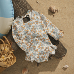 Långärmad baddräkt för flickor, tryckt, placerad på en träbit på en strand, med element runt omkring