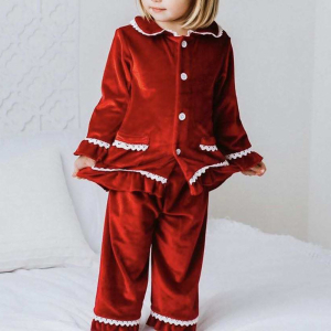 Liten blond flicka stående, klädd i julpyjamas i röd sammet