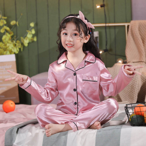 Ung flicka som sitter med benen i kors i rosa satinpyjamas