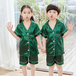 Ung flicka och pojke stående, en hand uppsträckt, klädda i gröna satinpyjamasar
