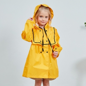 Liten leende blond flicka, stående, klädd i en gul regnjacka med huva