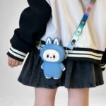 Flicka med en liten väska i silikon formad som ett Labubu-monster med kaninöron och färgglatt axelband